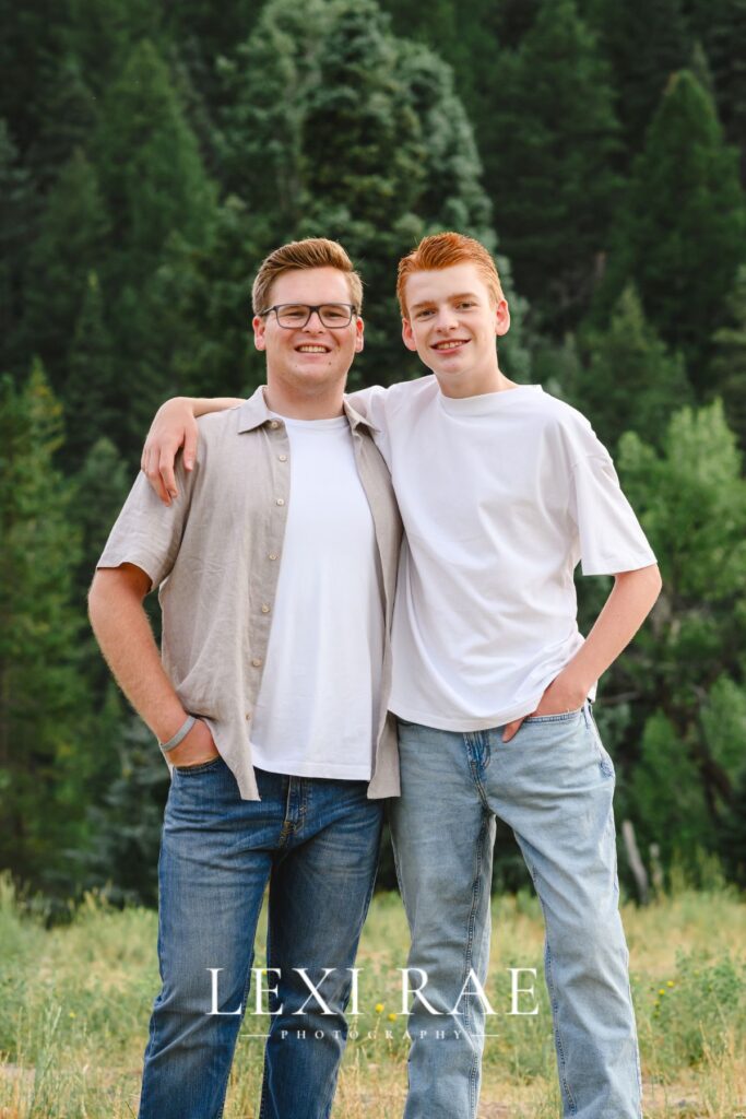 Two brothers posing for a photo in the Utah mountains. Both with hands in pockets and one arm around the other. 