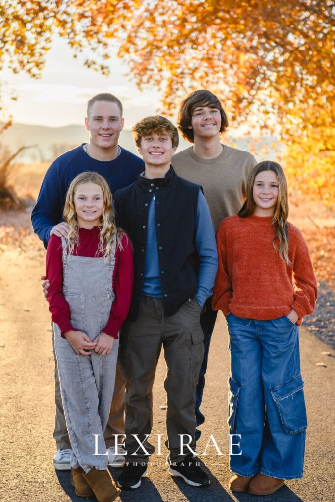 Five kids posing together in fall leaves. Wearing casual and comfortable clothes in Utah County. 