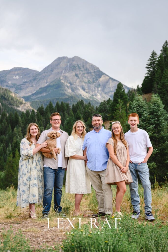 Family of 6 with dog posing for a photo in the Utah mountains. Family is all connected with hand placement. 