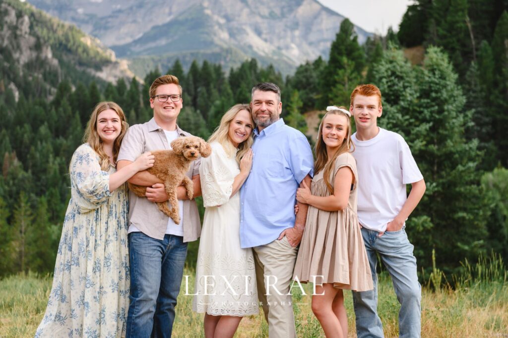 Family of 6 and one dog posing for a photo. Mountains in the background.