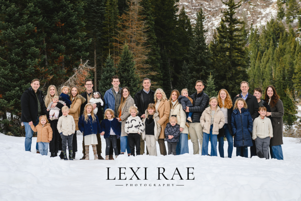 Large extended family photo up in the Utah mountains. Family is wearing comfortable and cozy winter outerwear of layers and coats. 